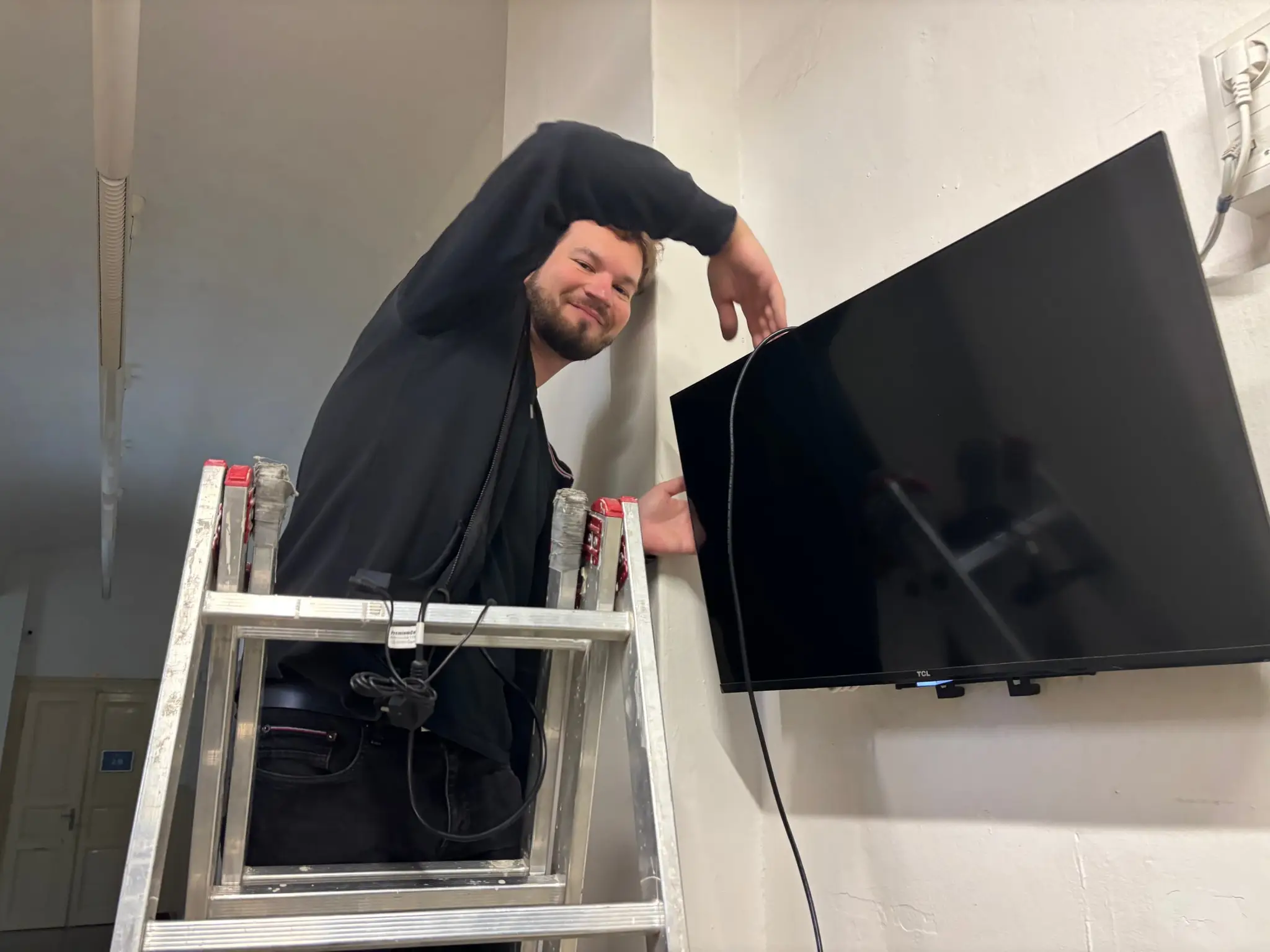 Technik na žebříku montuje televizi na zeď školy
